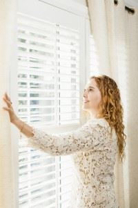 Woman pulling curtains back over window shutters