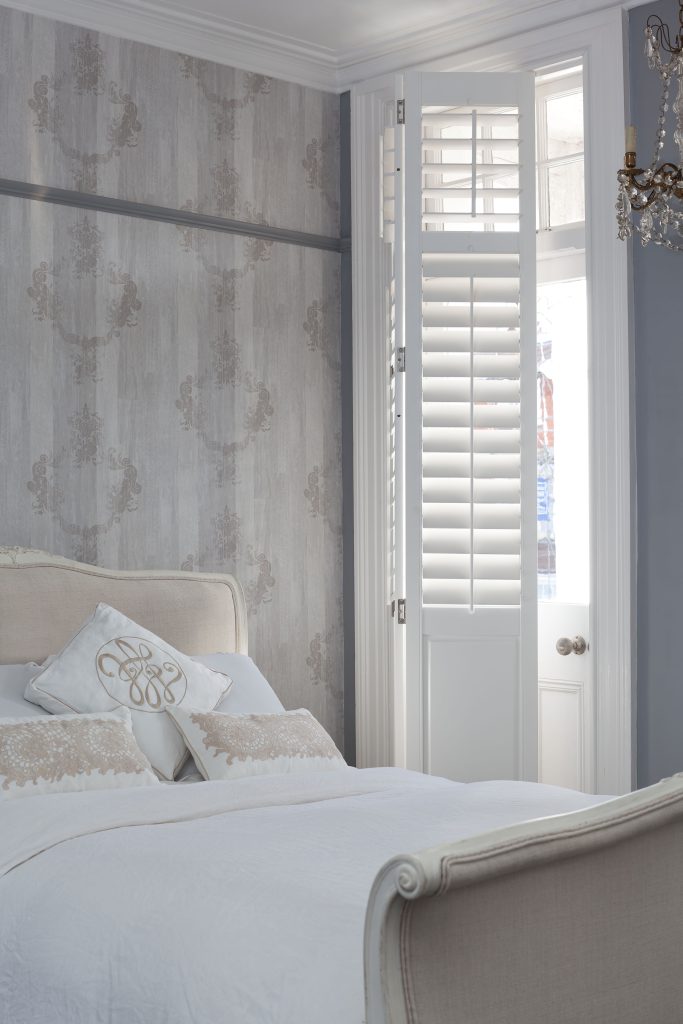 Solid wooden shutters in a chic bedroom in grey and white tones.