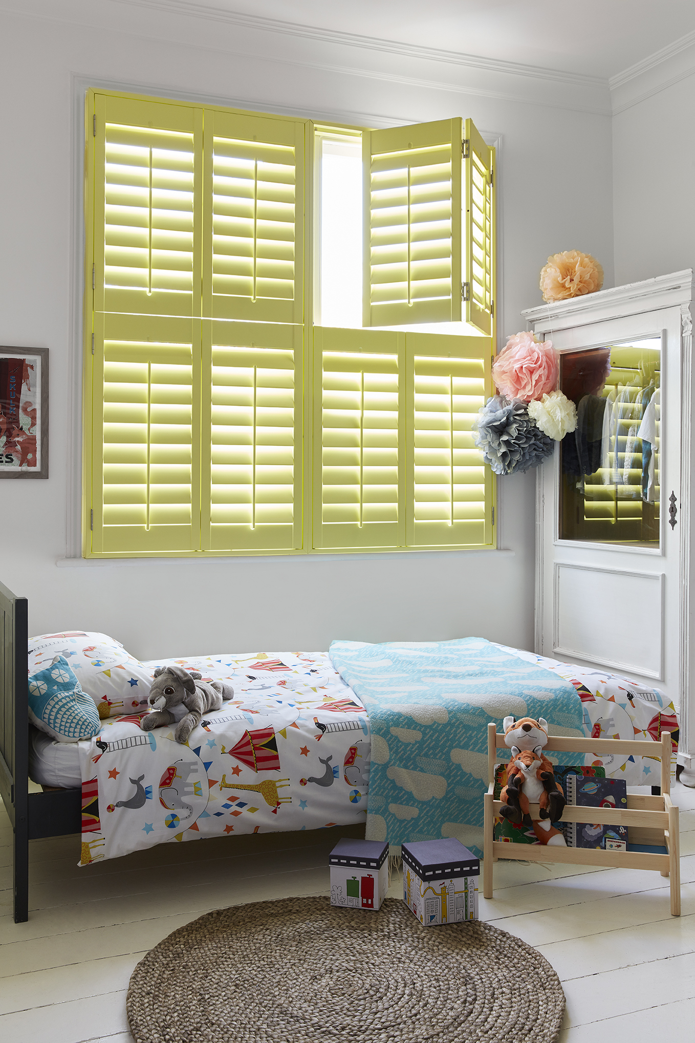 Yellow tier-on-tier window shutters in a children's room with a bed with circus patterns and toys. placeholder