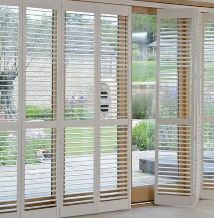 Tracked patio door shutters in white contrasting with a brick wall and opening to a garden