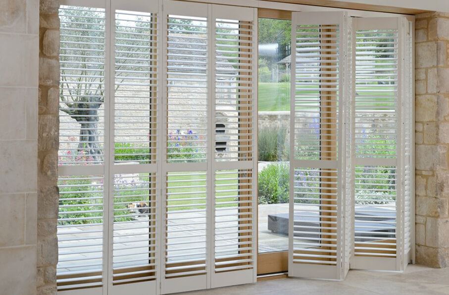 Tracked patio door shutters in white contrasting with a brick wall and opening to a garden
