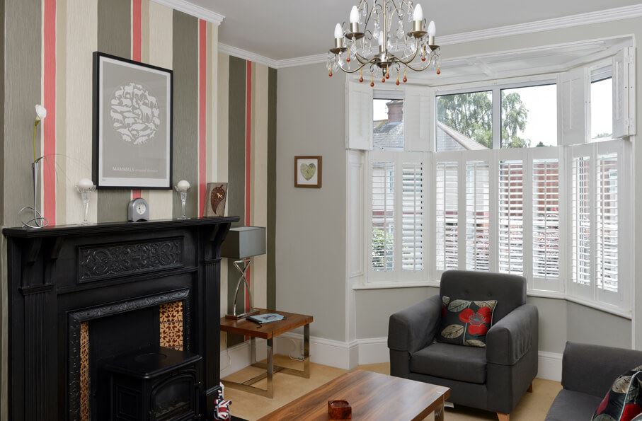 White cafe-style tier-on-tier shutters in a rustic living room with a fireplace.