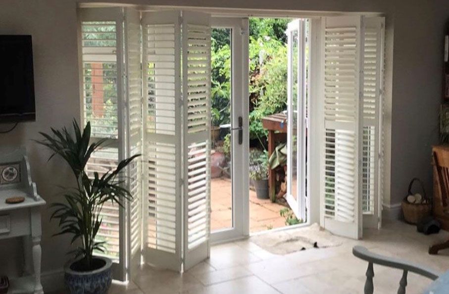 White tracked patio door shutters in a traditional room opening to a garden