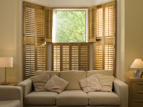 Wooden tier-on-tier bay window shutters in a beige living room.