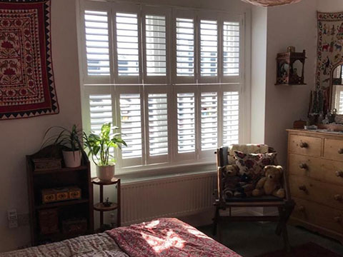 Tier-on-tier bedroom window shutters in white complementing a rustic style bedroom.