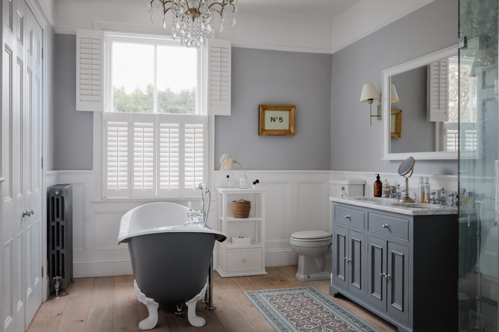 Bathroom with a classic grey decor, free standing bathtub and white tier-on-tier shutters.