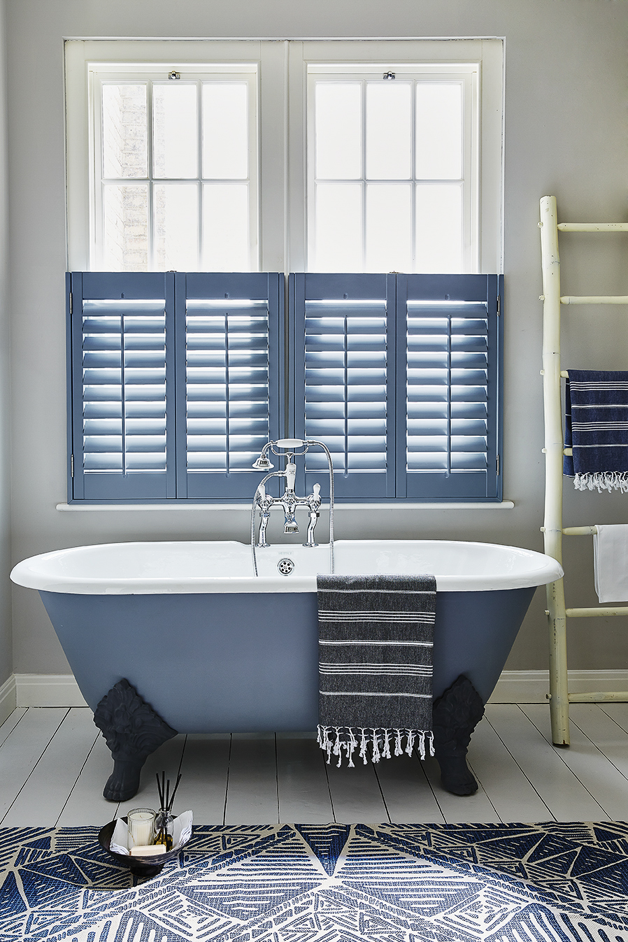 Bathroom shutters in blue with a blue free standing bathtub and modern decor. 