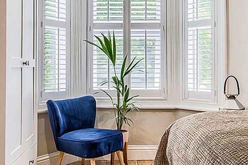 Bay window shutters in a bedroom with a blue chair.