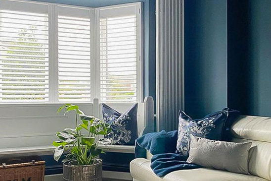 White bay window shutters contrasting with a blue wall in a living room.