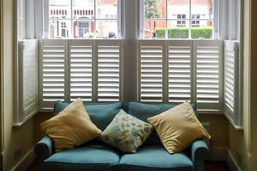 Café style shutters in a bay window behind a sofa.