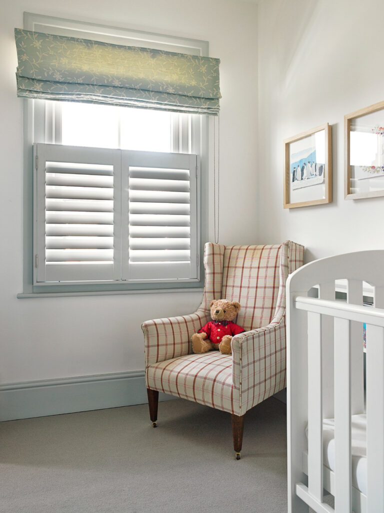 Café style shutters on a window in a nursery with a sofa and teddy bear in the corner of the room.