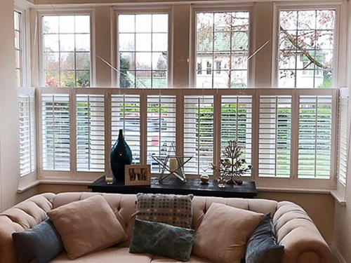 Café style shutters on a bay window in a snug with a sofa.