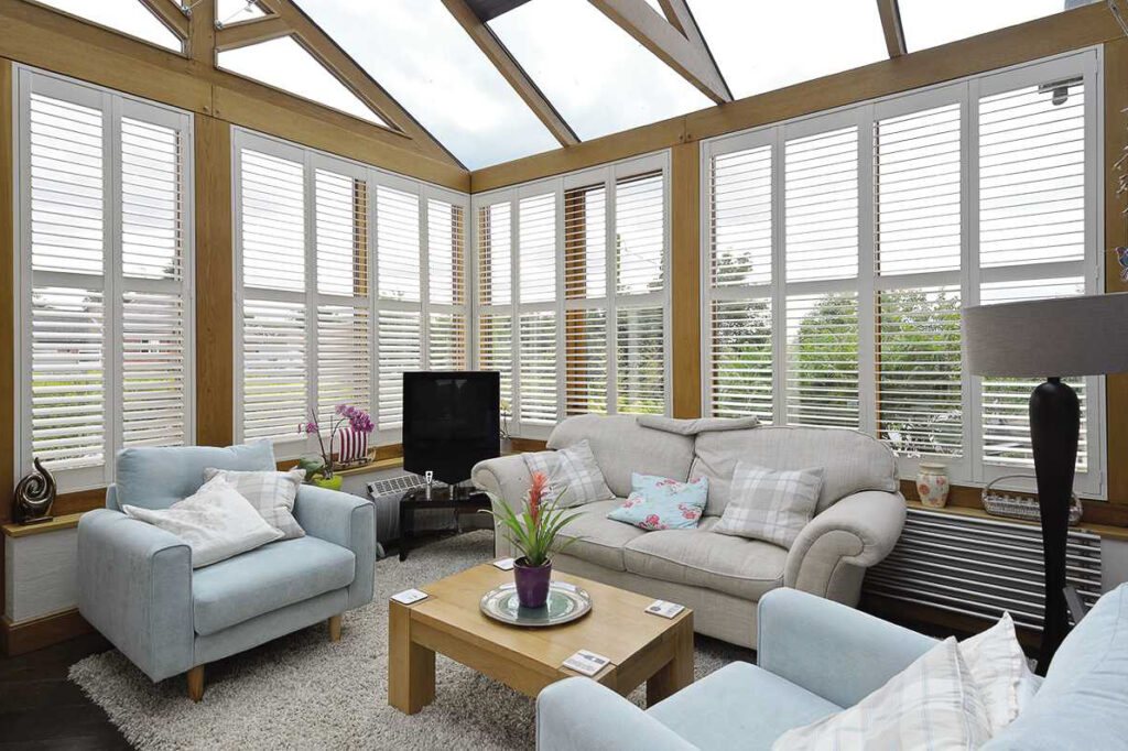 Conversatory shutters in a bright conservatory with sofas and a TV.
