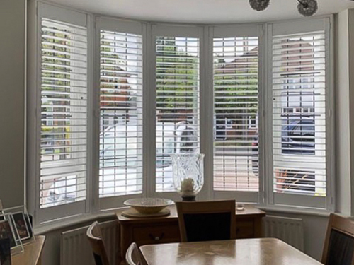 Dining room bay window shutters in white contrasting with dark wood furniture.